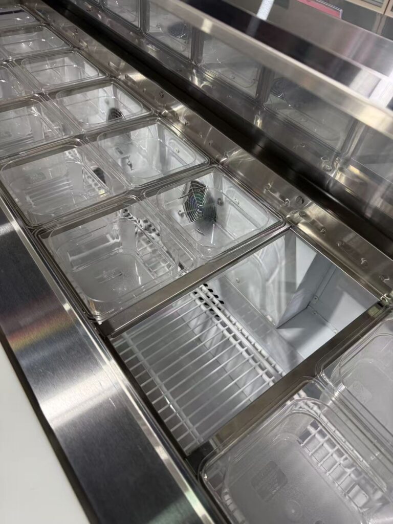 Close-up view of clear food-grade polycarbonate condiment GN pans in the top refrigerated rail of a pizza prep table