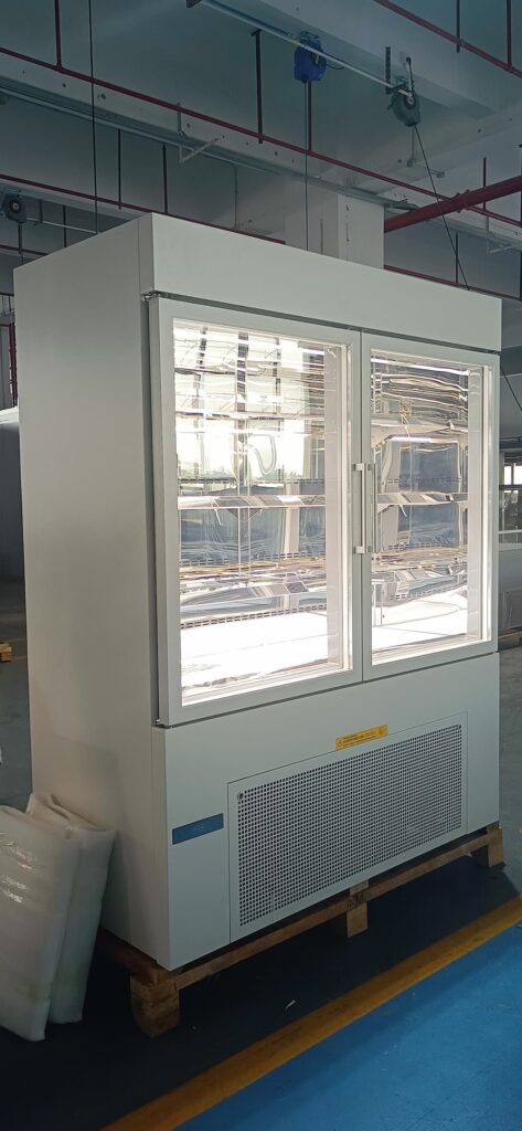 Upright white double door glass commercial display refrigerator in a factory setting